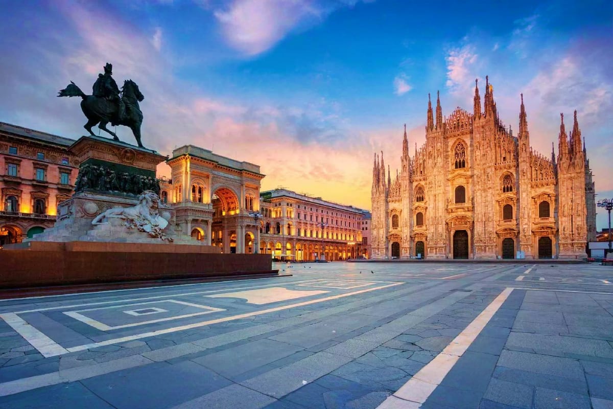 Milan Cathedral and Piazza del Duomo at sunset with equestrian statue and illuminated historic buildings