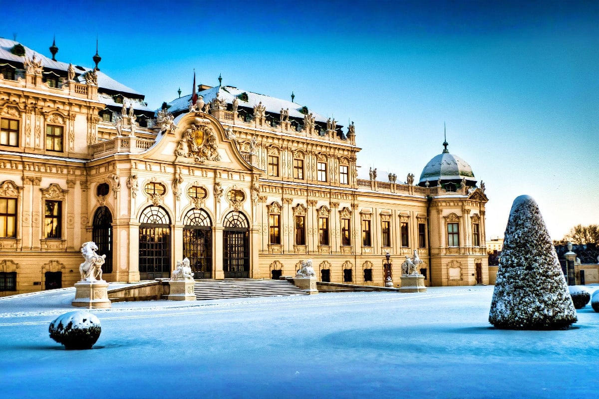 Baroque palace with snow-covered courtyard and ornate architectural details under clear blue winter sky in Vienna