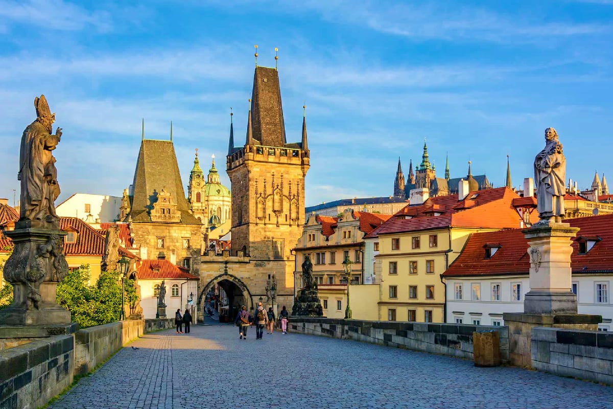 Charles Bridge in Prague with Gothic towers, statues, and historic old town buildings under blue sky
