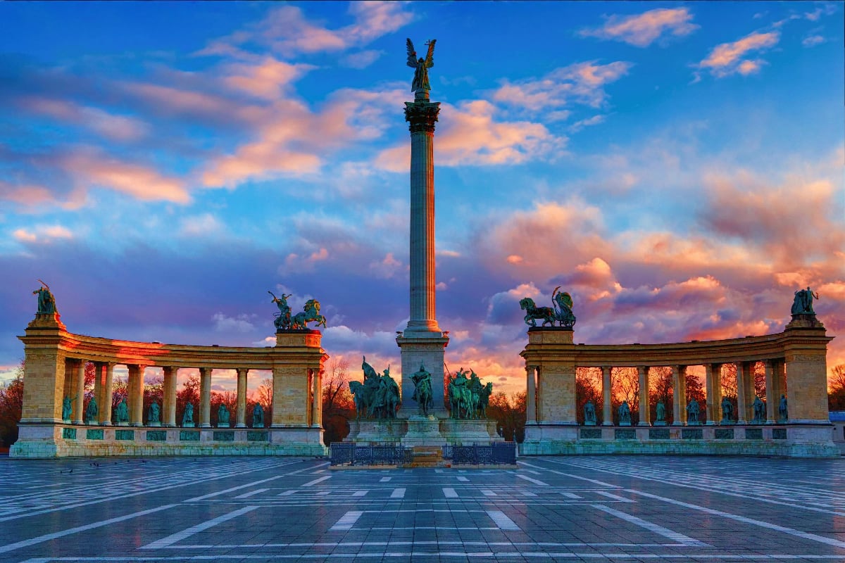 Heroes' Square in Budapest at sunset with central monument, colonnades, and equestrian statues under dramatic cloudy sky
