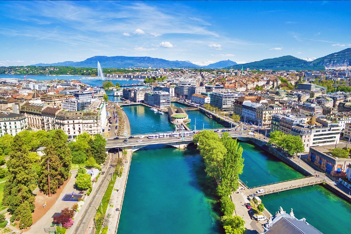 Aerial view of Geneva's turquoise lakes and bridges with surrounding buildings and mountains in background