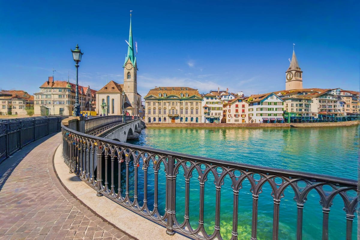 Zurich riverfront with churches and historic buildings reflected in turquoise water, ornate iron railing in foreground