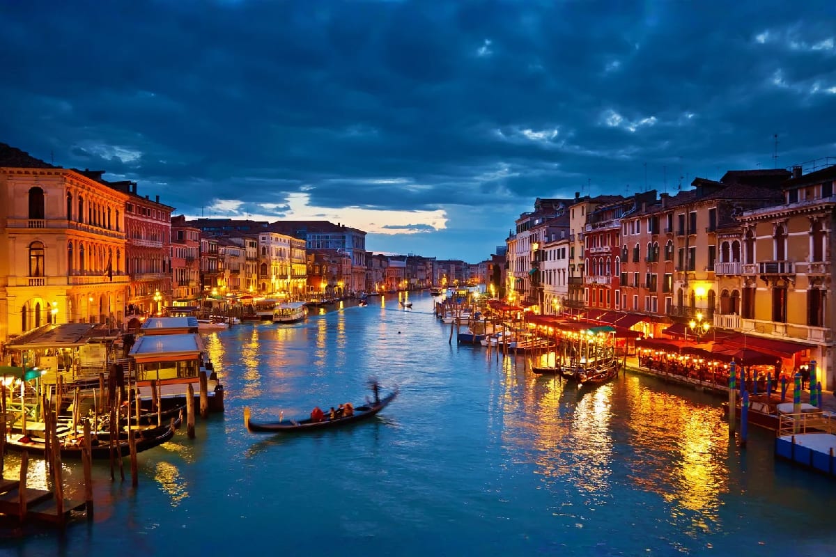 Grand Canal in Venice at dusk with illuminated Renaissance buildings, gondola, and reflections on water