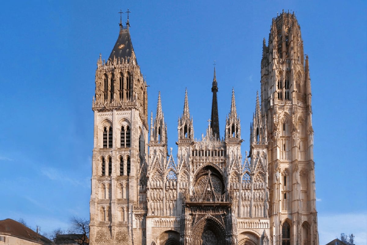 Rouen Cathedral's ornate Gothic façade with twin towers and intricate stone spires against a clear blue sky