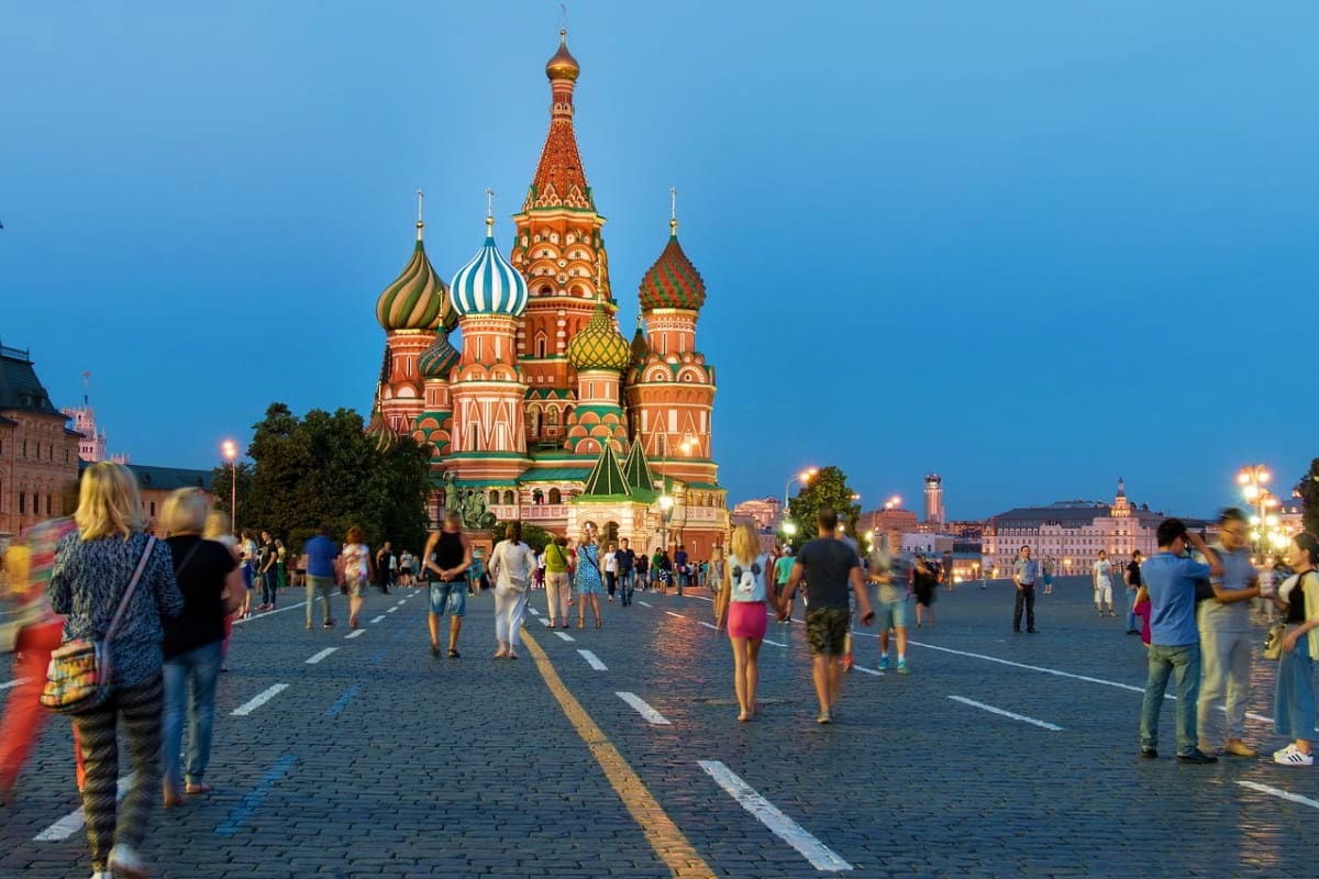 Saint Basil's Cathedral in Red Square, Moscow at dusk with tourists walking on the cobblestone plaza and blue evening sky