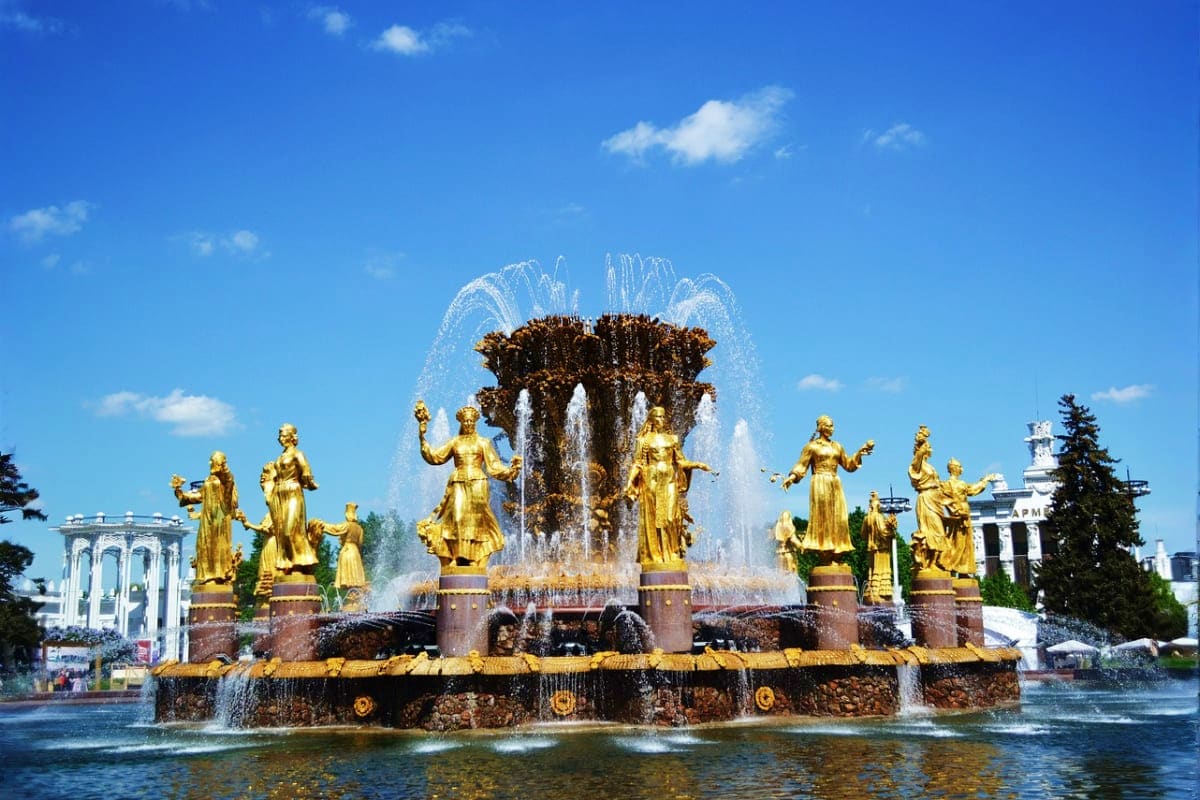 Golden statues and fountain at VDNKh exhibition center in Moscow with blue sky and white pavilions in background