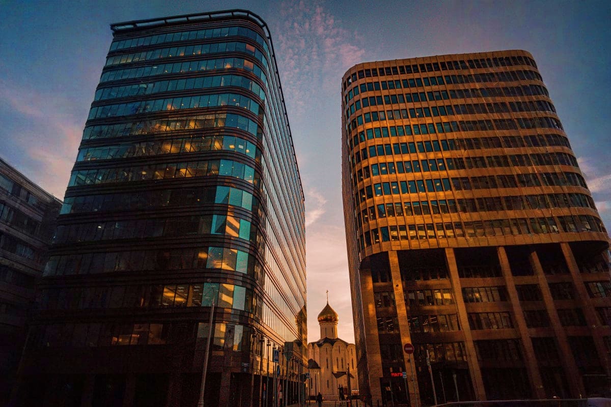Modern glass office buildings at sunset with Orthodox church with golden dome visible between them in Moscow cityscape