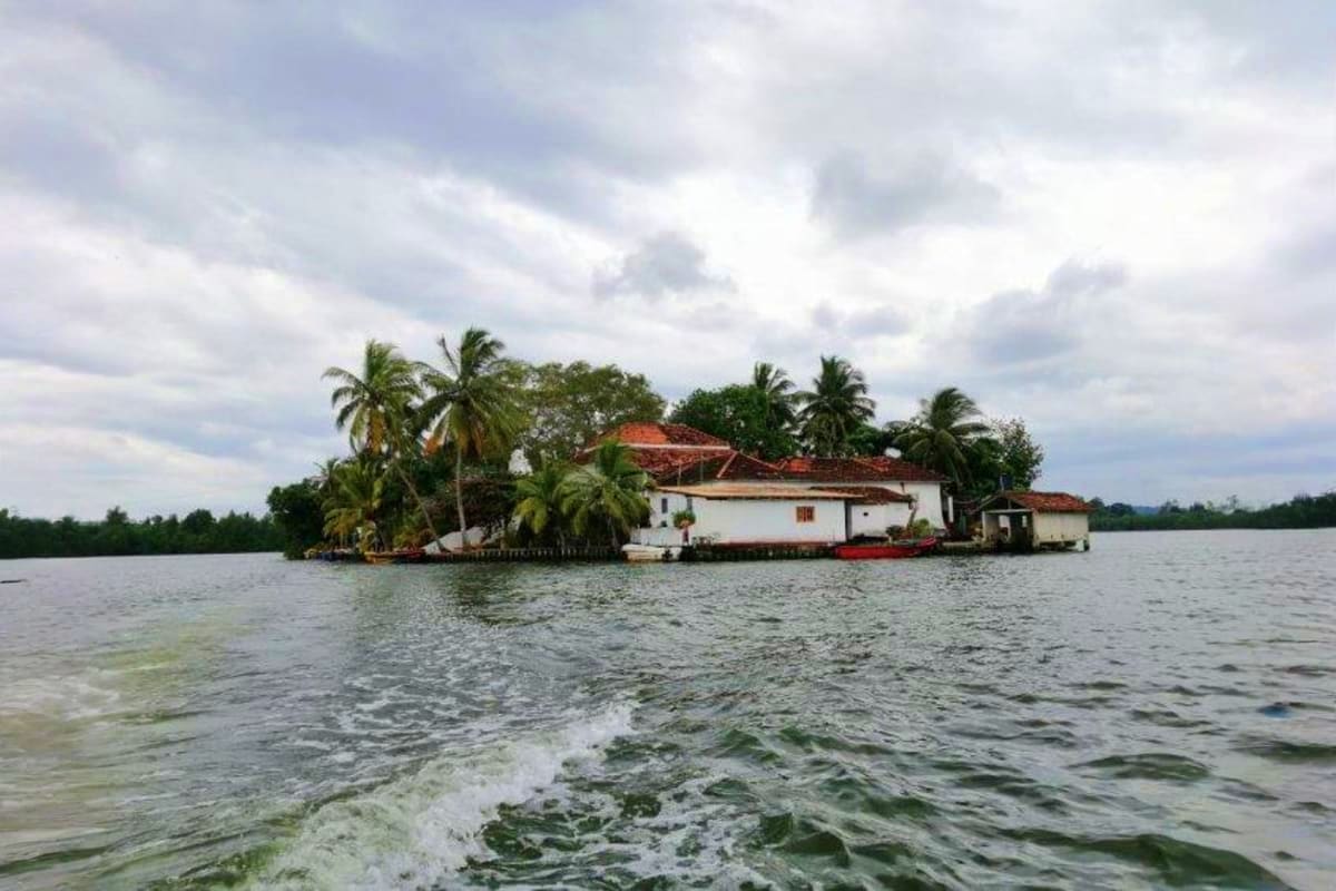 Waterfront colonial house with red tile roof surrounded by palm trees on an island in Sri Lanka backwaters