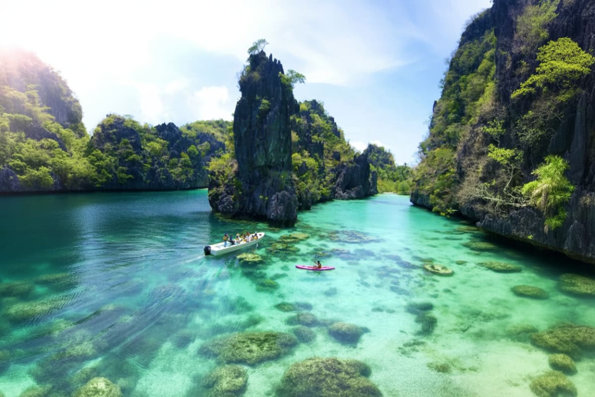 Turquoise lagoon surrounded by towering limestone cliffs with lush green vegetation and tourists in boats exploring the clear