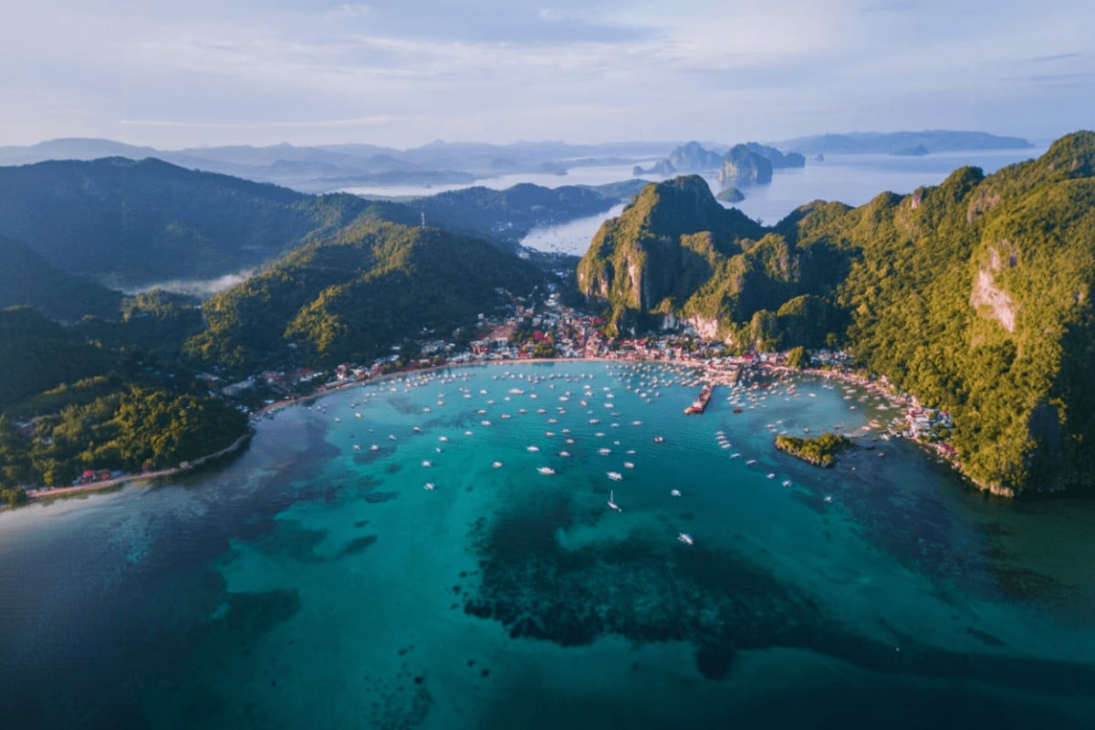 Aerial view of El Nido bay with turquoise water, limestone cliffs, boats, and surrounding forested mountains in Palawan, Phil