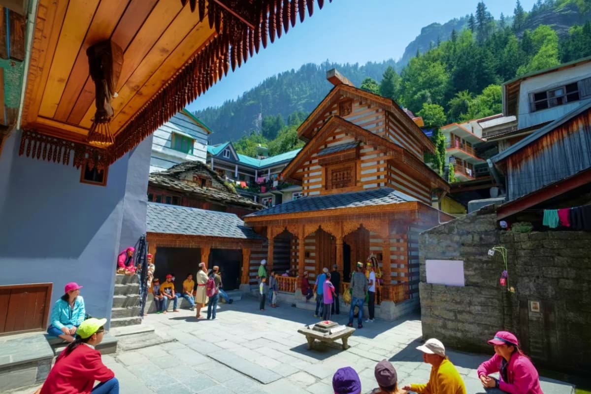 Traditional wooden log houses with ornate architecture in a mountain village courtyard surrounded by pine forests and snow-ca