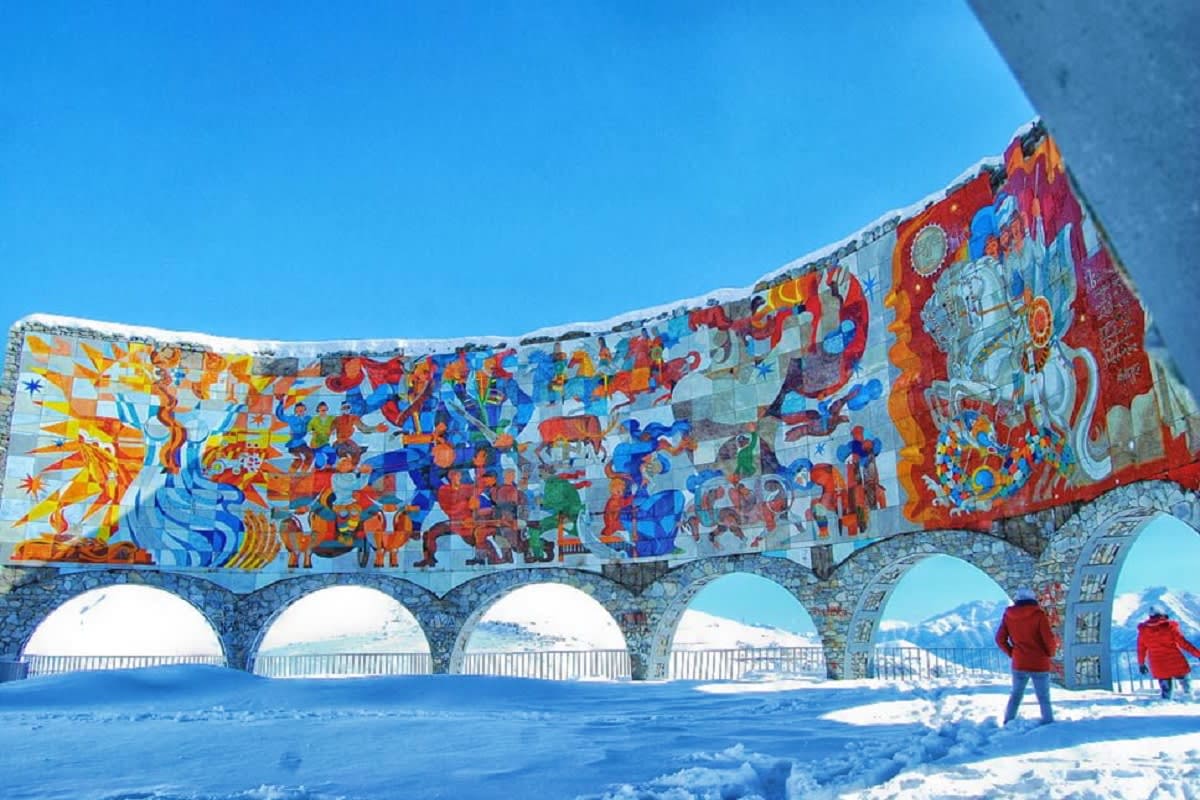Colorful mosaic mural on stone bridge with arches in snowy mountain landscape, Georgia