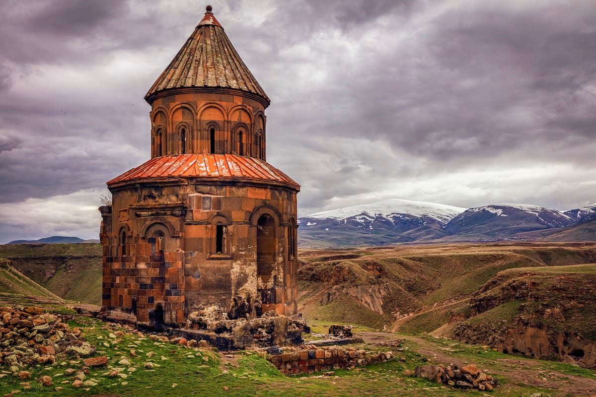 Ancient Armenian chapel with conical roof in mountainous landscape under cloudy sky