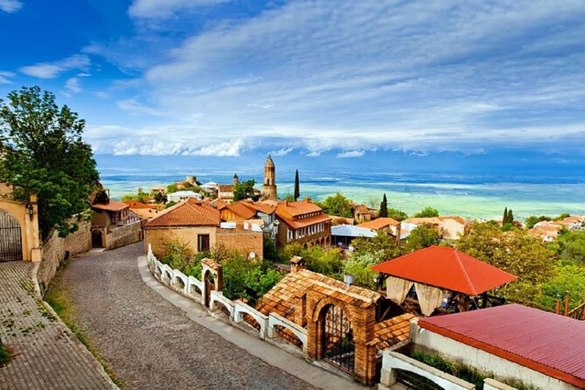 Sighnaghi village perched on hillside with terracotta roofs, church bell tower, and sweeping valley views toward snow-capped 