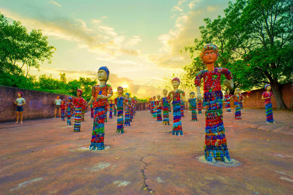 Colorful yarn-wrapped figurines displayed in an outdoor courtyard with trees and golden sunset sky, Himachal Pradesh folk art
