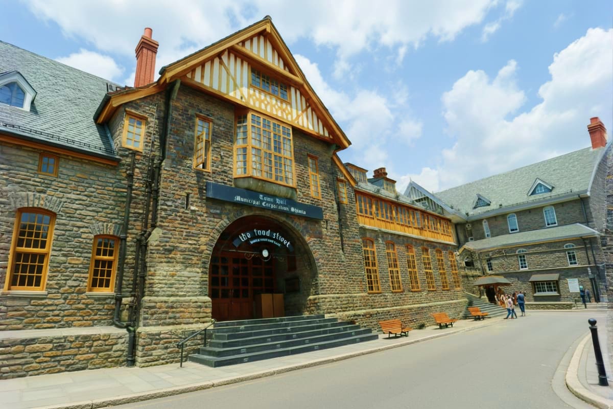 Solang And Kufri Adventure Tour The Himachal Highlights Historic stone building with half-timbered gable featuring arched entrance and yellow window frames in courtyard setting