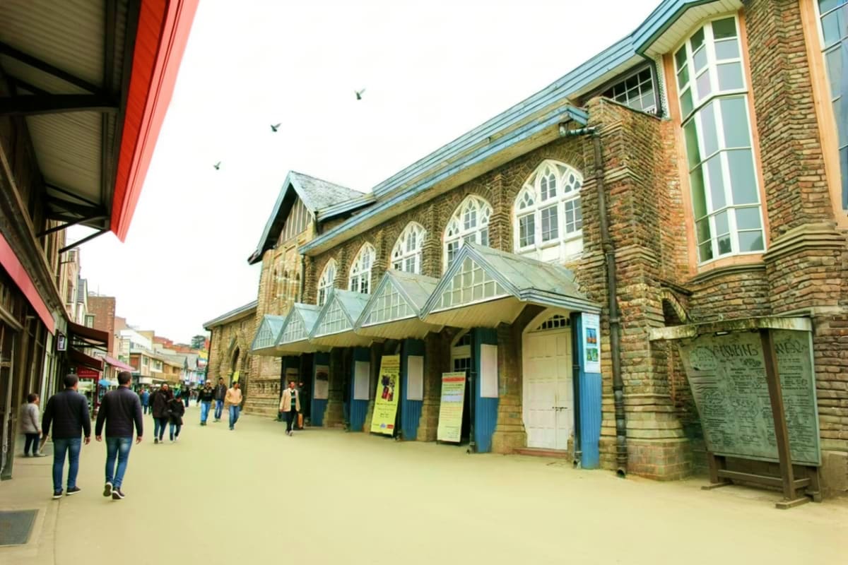 Solang And Kufri Adventure Tour The Himachal Highlights Victorian-era stone building with arched windows and blue trim on a pedestrian shopping street with visitors walking by