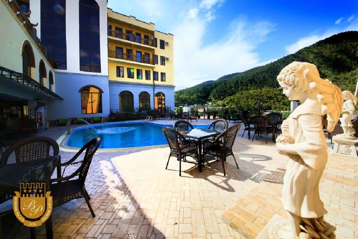 Luxury resort pool deck with blue swimming pool, dining chairs, white angel statues, and colorful buildings overlooking fores