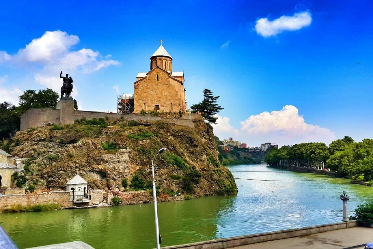 Metchi Church perched on rocky cliff overlooking Mtkvari River in Tbilisi, Georgia with equestrian statue and blue sky