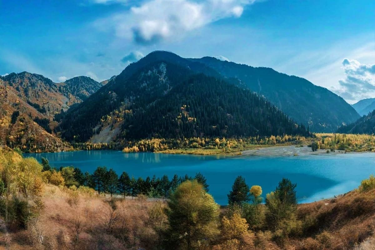 Turquoise alpine lake surrounded by forested mountains and golden larch trees in Almaty region, Kazakhstan