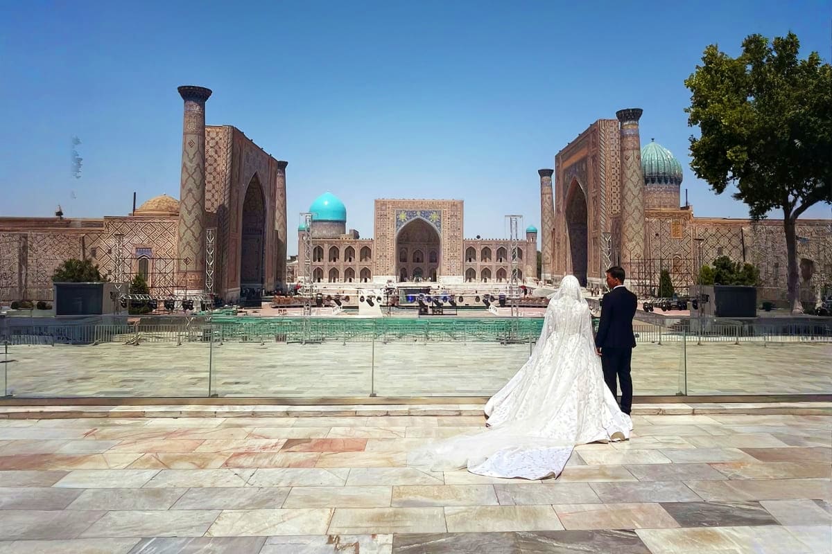 Bride and groom at Registan Square in Samarkand, Uzbekistan with ornate Islamic architecture and turquoise domes