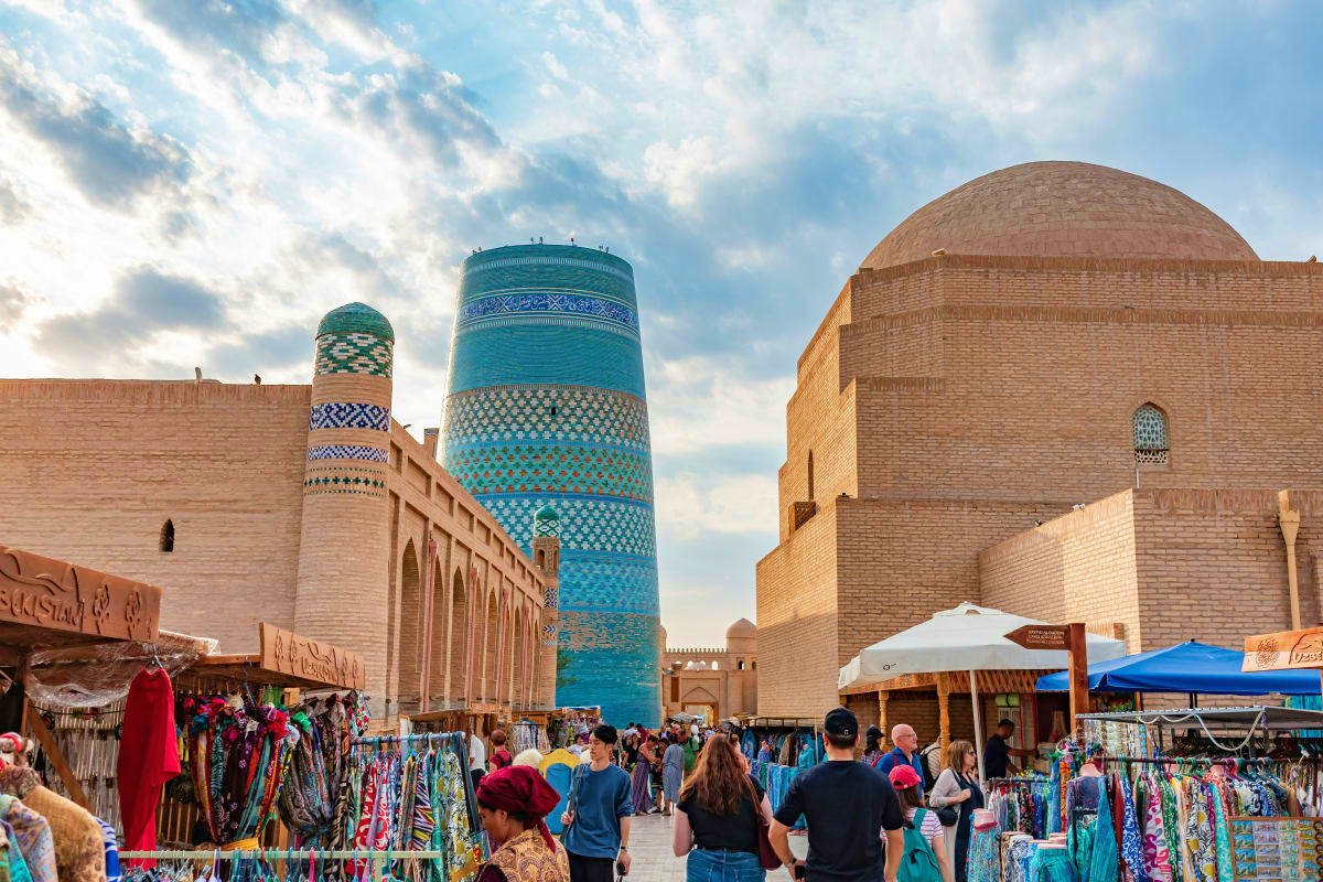 Bustling bazaar in Khiva, Uzbekistan with turquoise Kalta Minor minaret and historic brick buildings under blue sky
