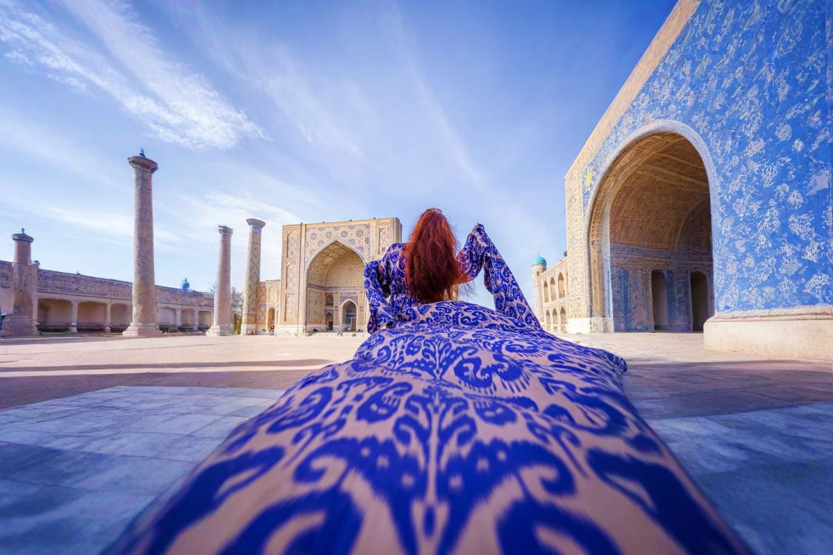 Woman in blue patterned dress lying on tiled courtyard at Registan mosque complex in Samarkand, Uzbekistan