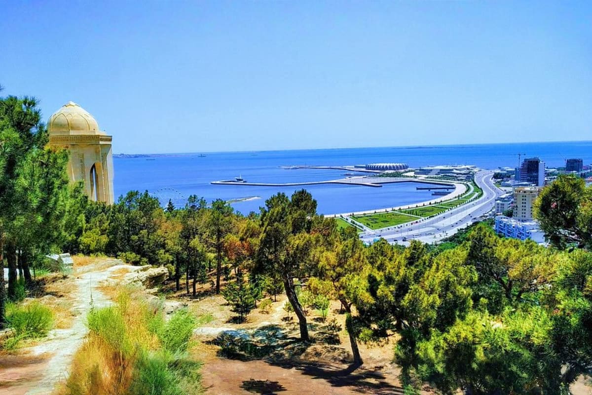 Panoramic view of Baku cityscape with golden-domed mosque, coastal promenade, and Caspian Sea under clear blue sky