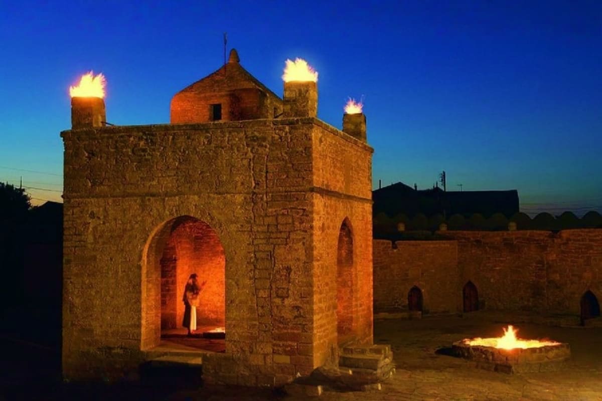 Ancient stone fire temple at dusk with burning flames on top towers and courtyard, Baku Azerbaijan