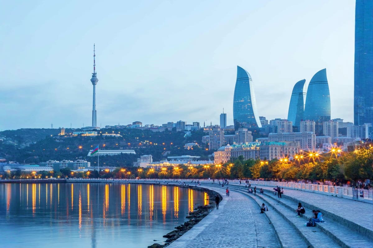 Baku cityscape at dusk with illuminated Flame Towers, Maiden Tower, TV tower, and waterfront promenade with people walking al