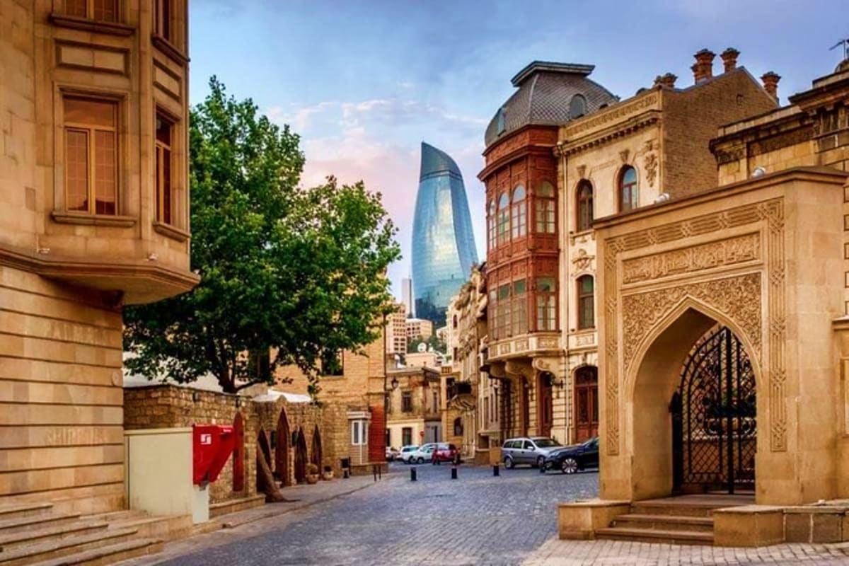 Historic old town street in Baku with traditional Azerbaijani architecture, Flame Towers skyscraper, and ornate arched gatewa