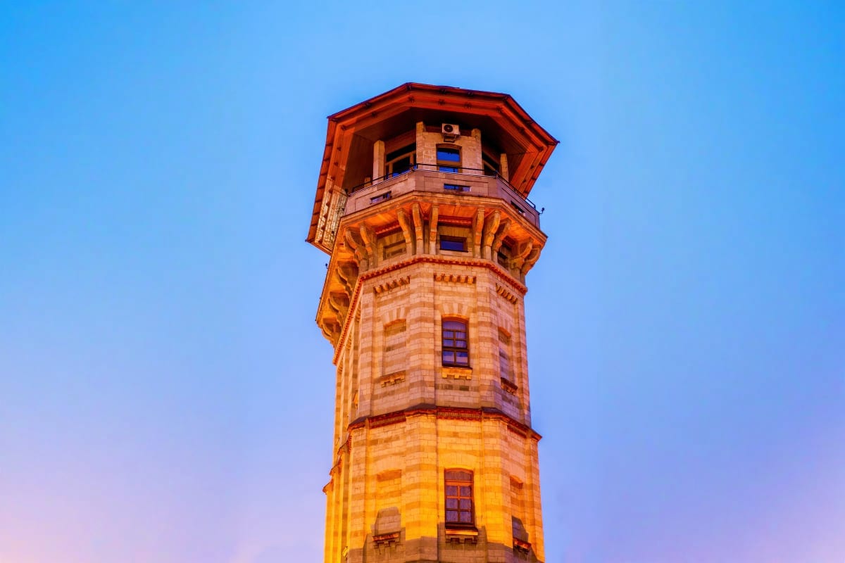 Historic stone tower with red roof lit by golden hour light against blue sky, iconic landmark architecture