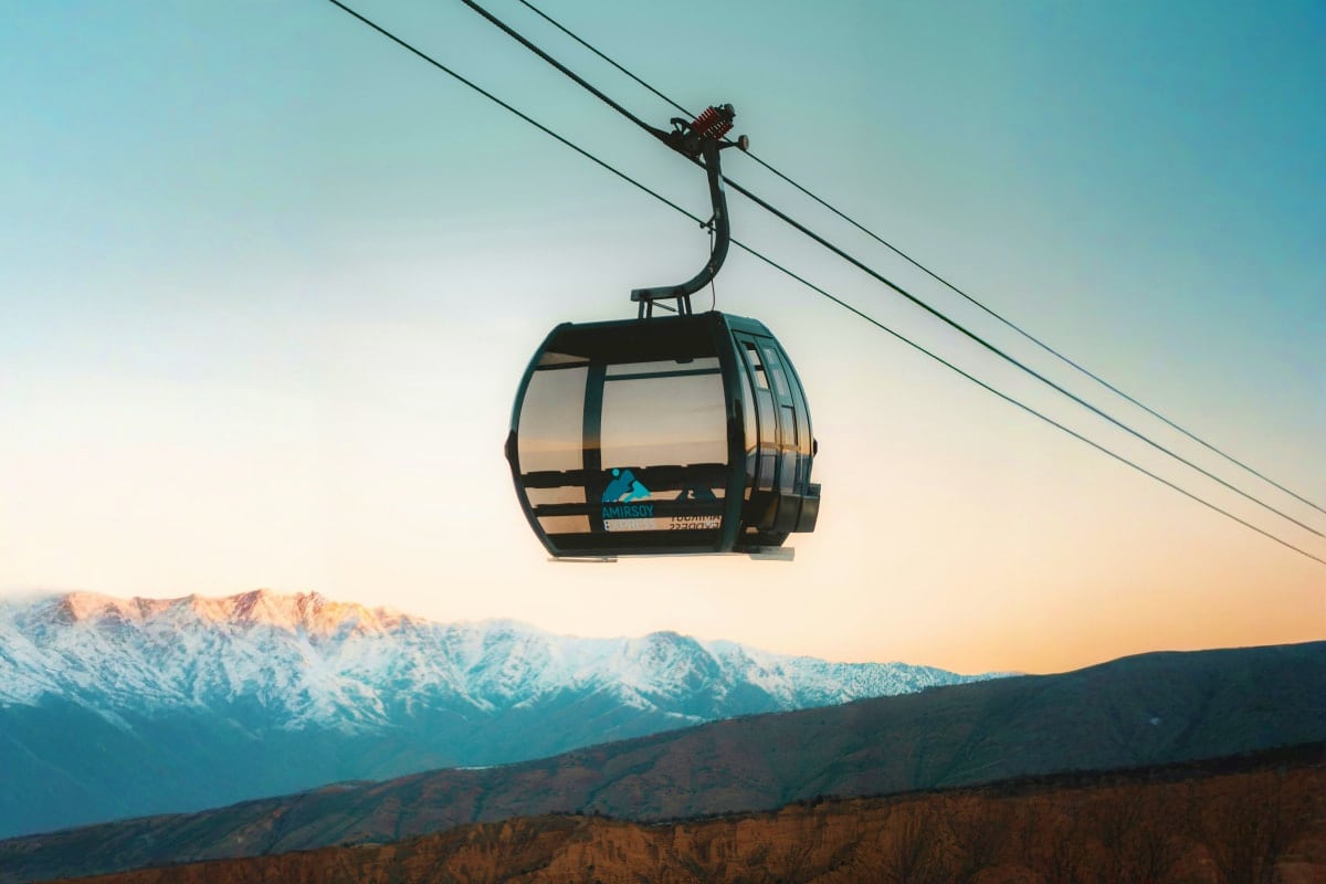 Cable car suspended above snow-capped mountains at sunset in Uzbekistan