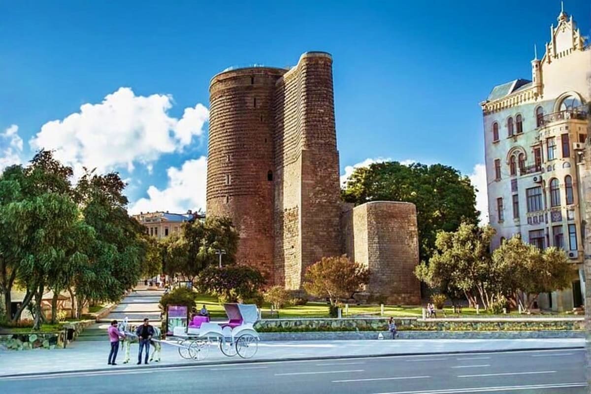 Maiden Tower historic landmark in Baku with surrounding park, trees, and classical architecture buildings under clear blue sk
