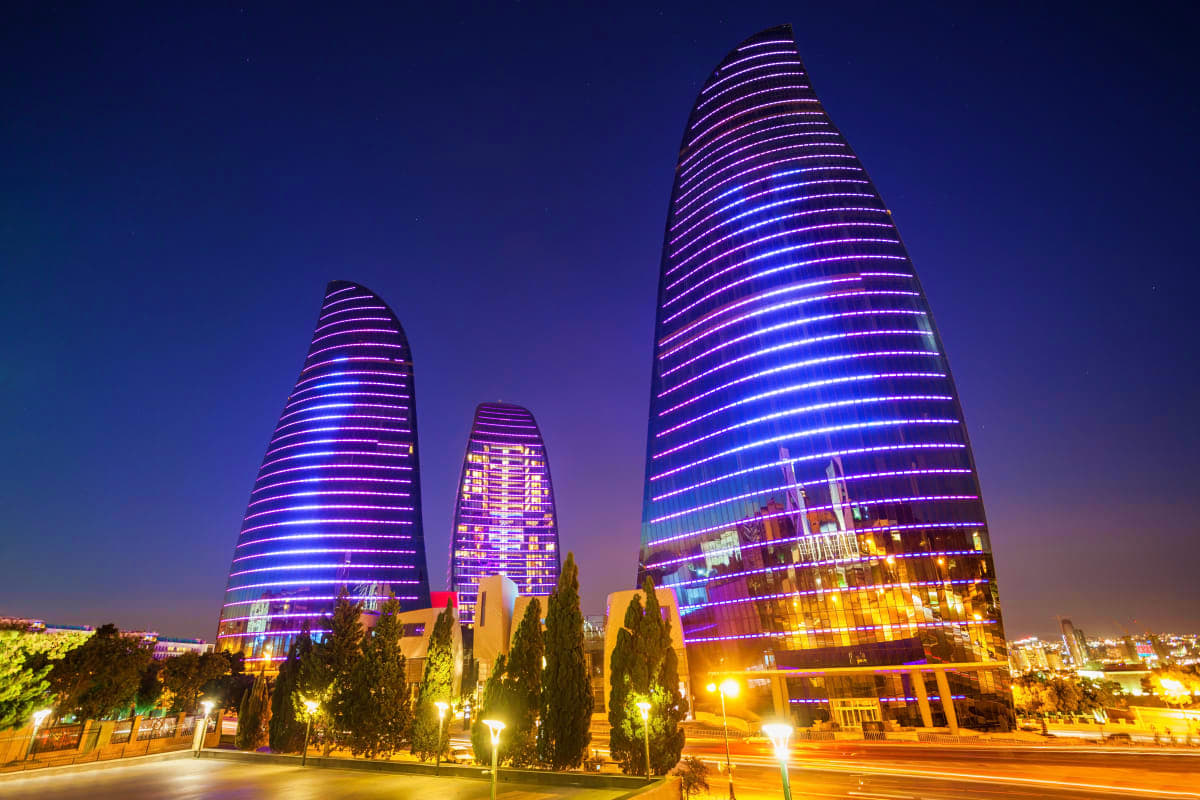 Modern illuminated skyscrapers with purple and blue LED lighting at night in Baku city center with cypress trees and street l