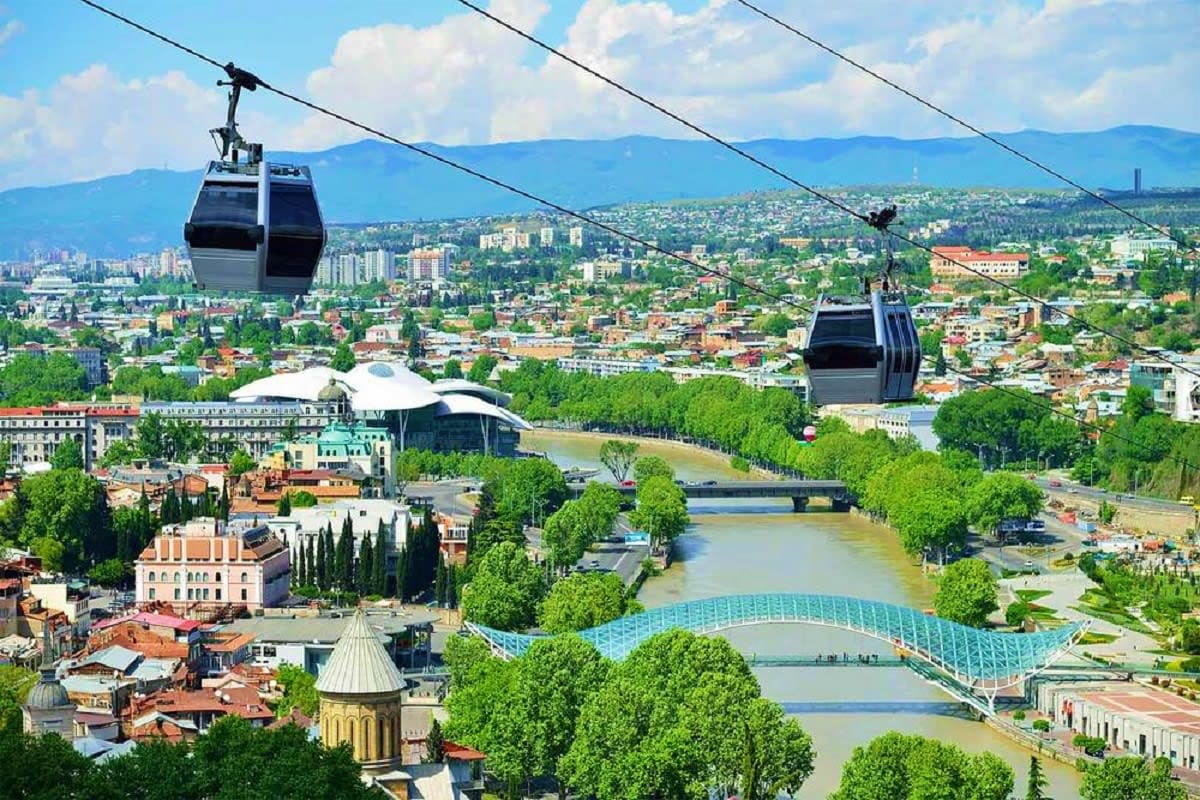 Aerial cable car view of Tbilisi cityscape with Metekhi Church, Mtkvari River, and mountain backdrop
