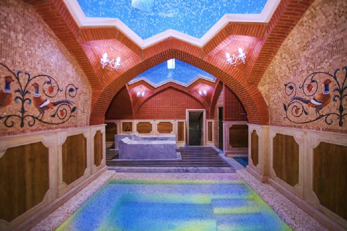 Interior of traditional Georgian bathhouse with red brick arches, decorative wall panels, blue mosaic ceiling, and steaming p