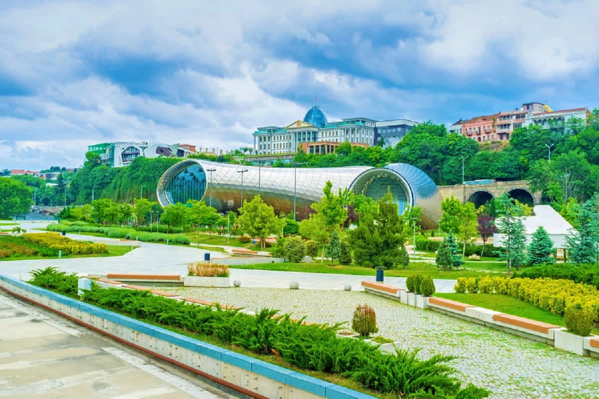 Modern riverside park in Tbilisi with distinctive cylindrical glass structures, landscaped gardens, and historic architecture