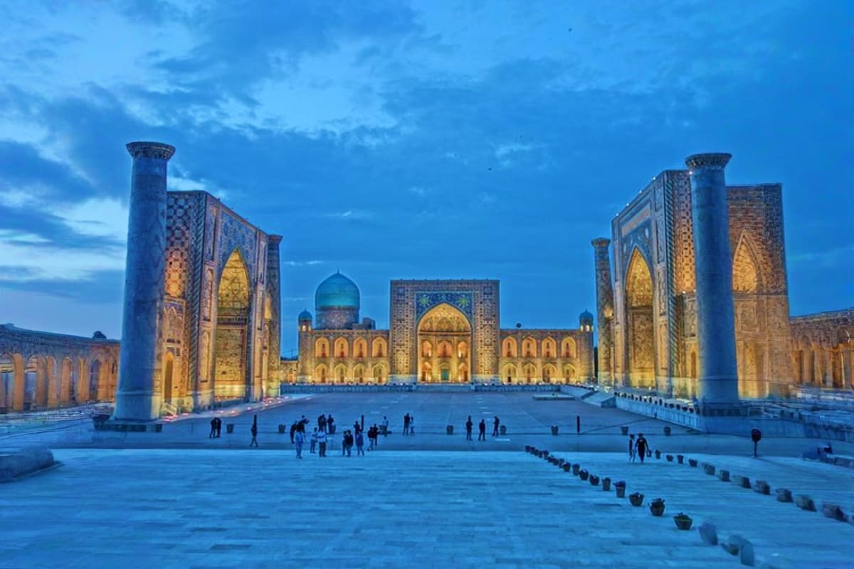 Registan Square in Samarkand at twilight, showcasing three illuminated madrasas with intricate tilework and tall minarets, vi