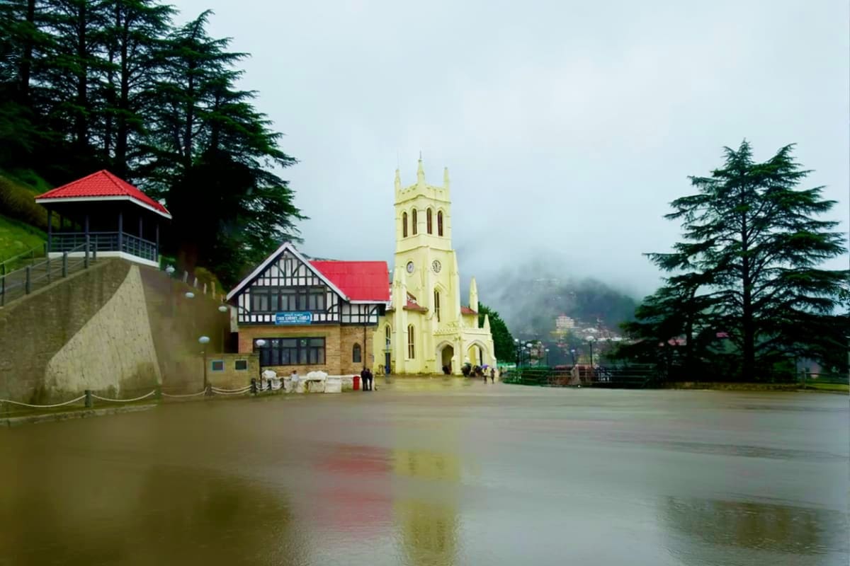 Cream-colored church with red roof reflected in still water at Shimla, surrounded by cedar trees and misty mountains in Himac