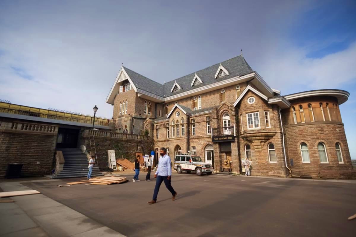 Historic stone building with slate roof and multiple gables in a courtyard setting with visitors and construction materials