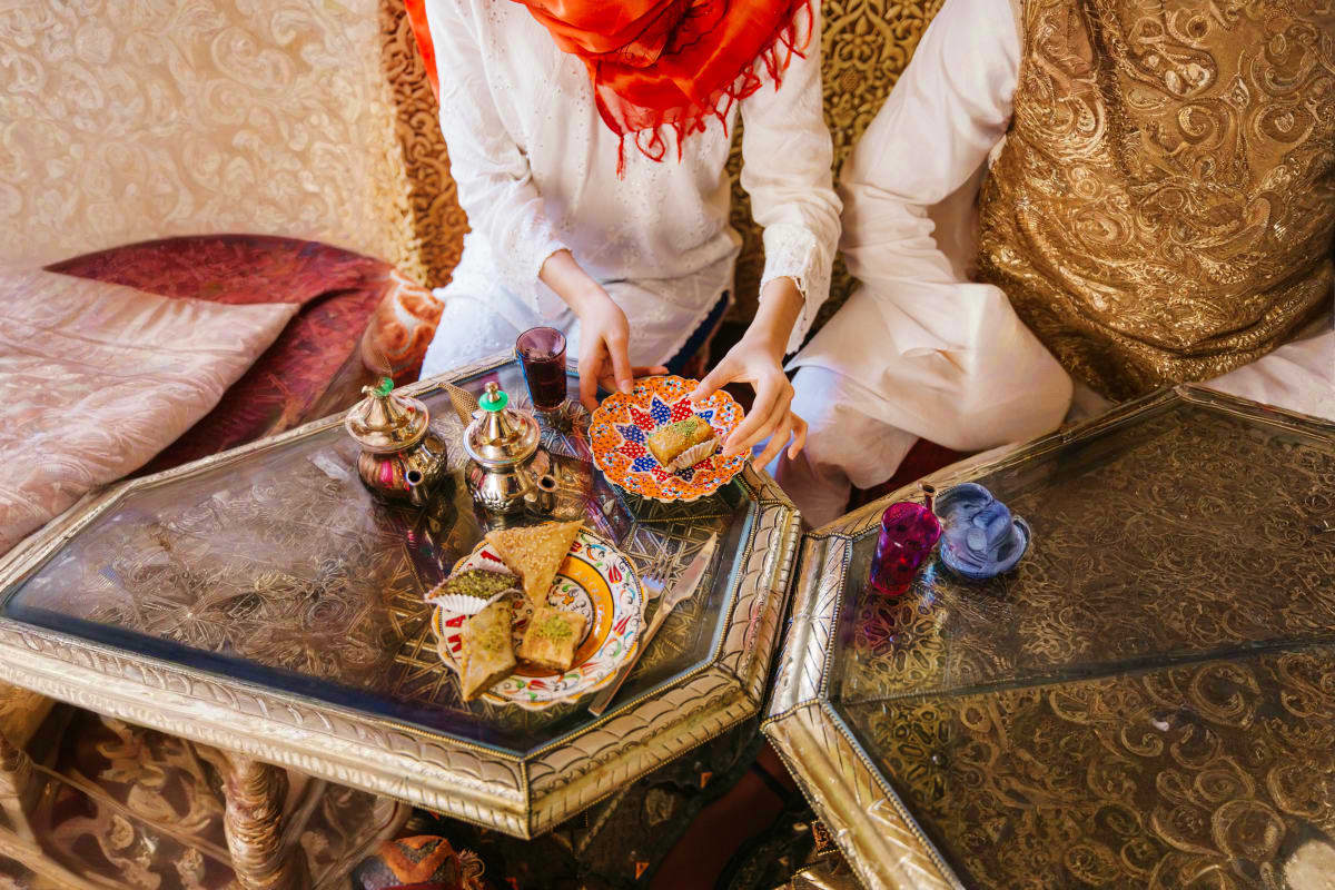 Baku & Gabala Love Escape Woman in white traditional dress serving tea and pastries on ornate table with Moroccan decor and cushioned seating