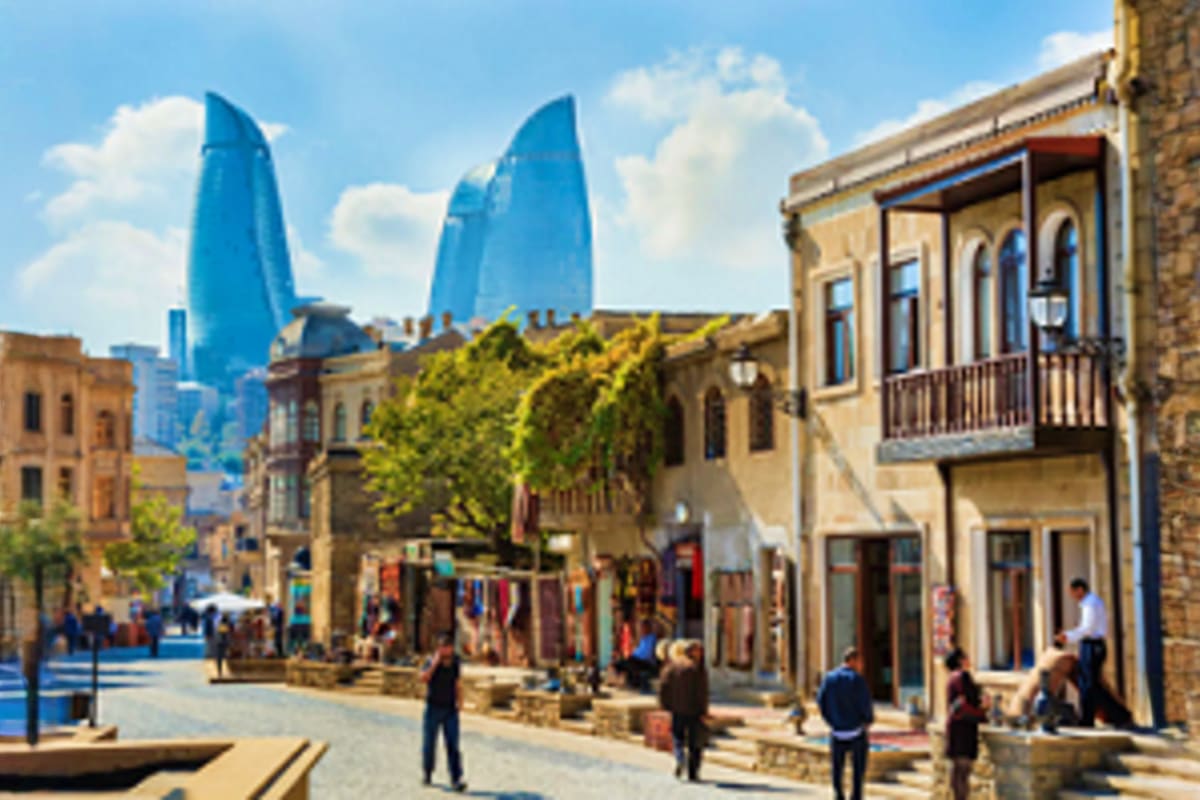 Baku & Gabala Love Escape Old city street in Baku with historic stone buildings and modern blue-glass towers visible in the background under blue sky