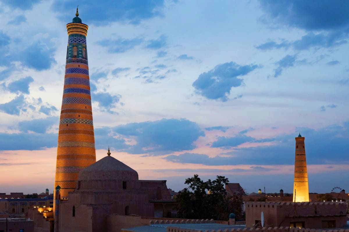Illuminated minarets and mosque with geometric tile patterns at dusk in Khiva, Uzbekistan's historic old city