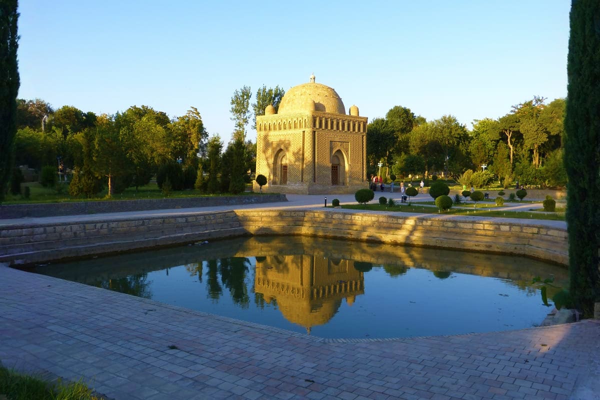 Ismail Samani Mausoleum with golden dome reflected in a reflecting pool, surrounded by manicured gardens and cypress trees in