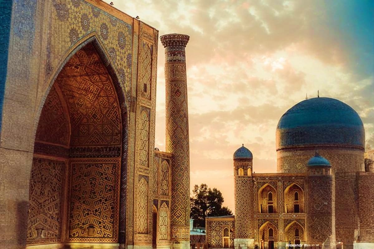 Historic Islamic architecture in Samarkand featuring ornate blue dome, decorated minaret, and carved wooden door with geometr
