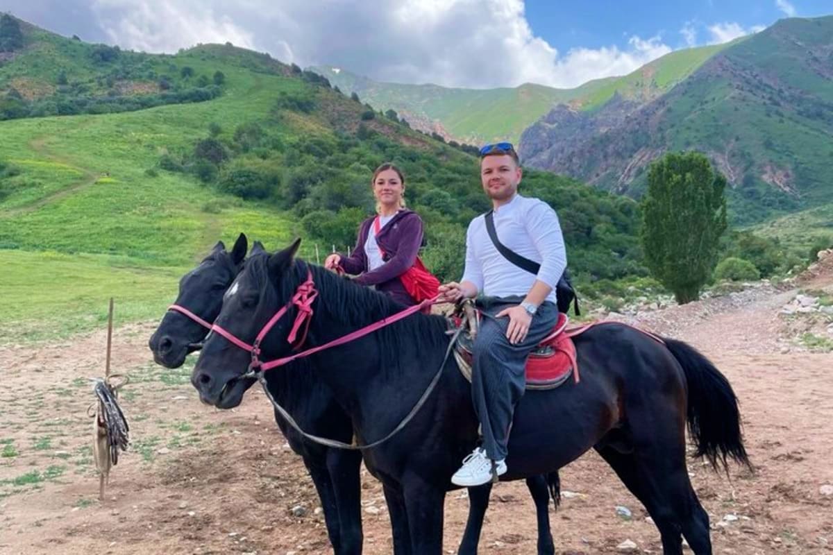 Couple horseback riding in lush mountain valley with green hills and rocky terrain in Uzbekistan