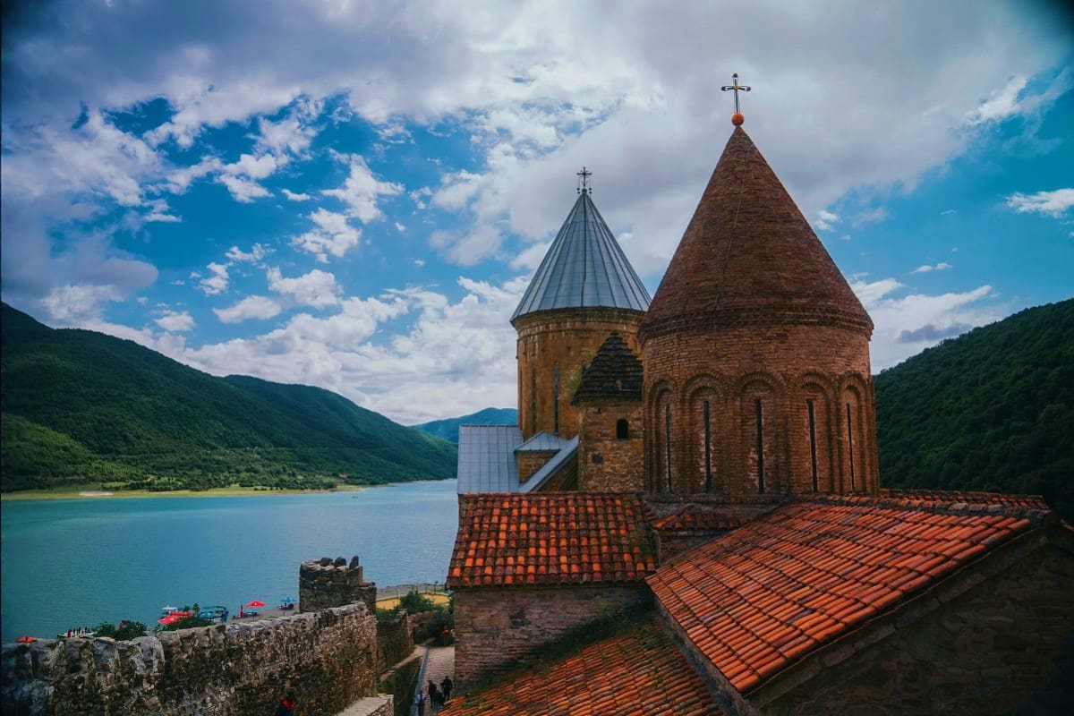 Akdamar Church with twin stone towers and red-tiled roofs overlooking turquoise Lake Sevan, surrounded by green mountains und