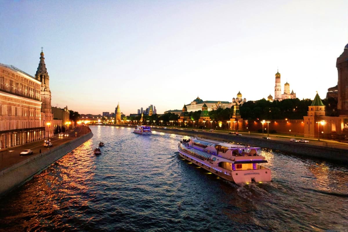 Moscow River at twilight with illuminated Kremlin walls, historic buildings, golden domes, and passenger river cruise boats