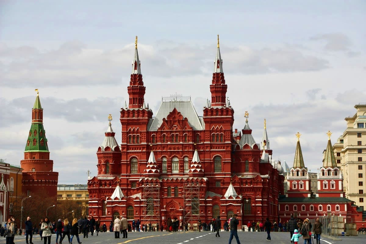 State Historical Museum with distinctive red brick towers and spires in Red Square, Moscow, with tourists walking in the plaz